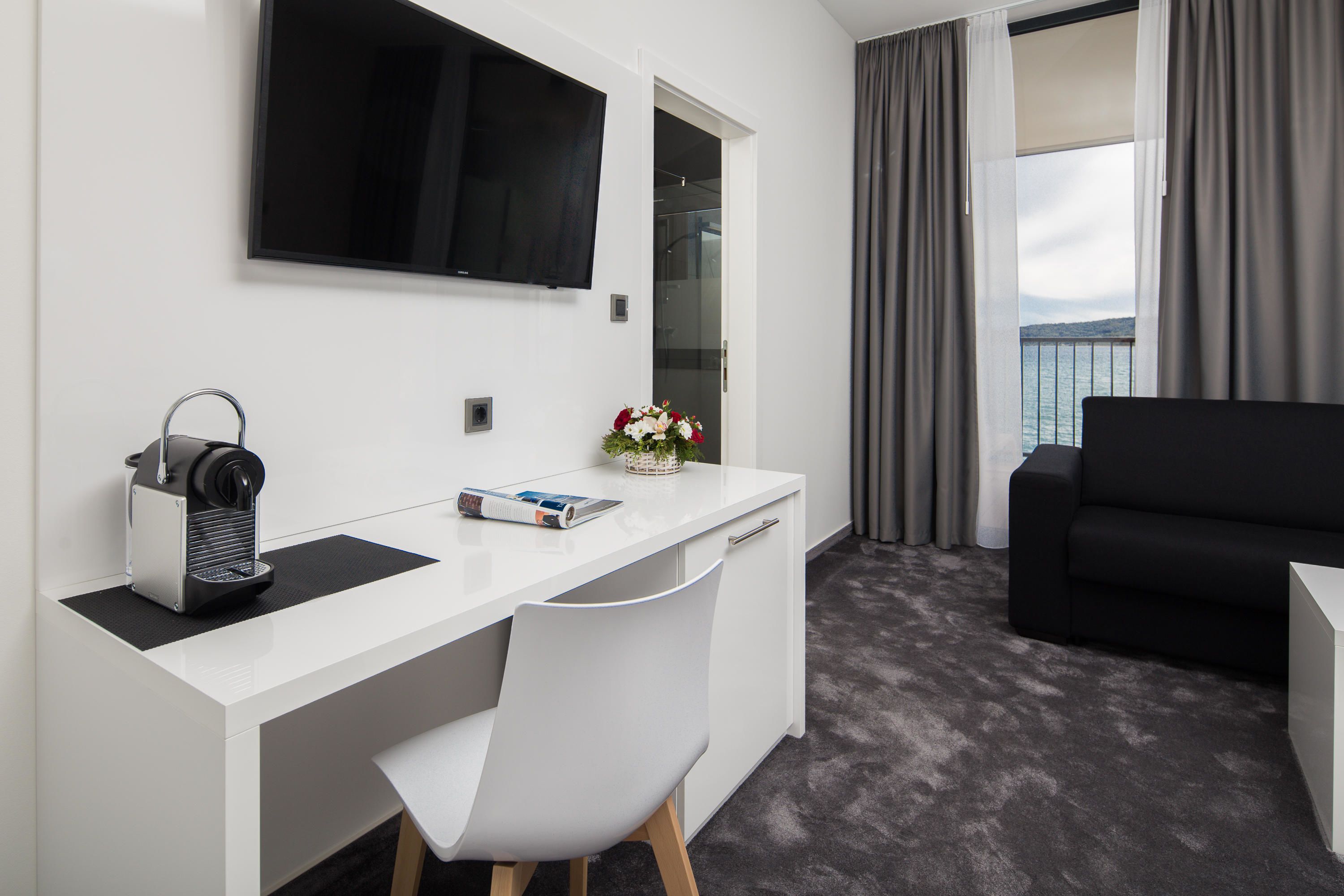Een moderne hotelkamer met een wit bureau, een zwarte bank, een flatscreen televisie en uitzicht op zee.