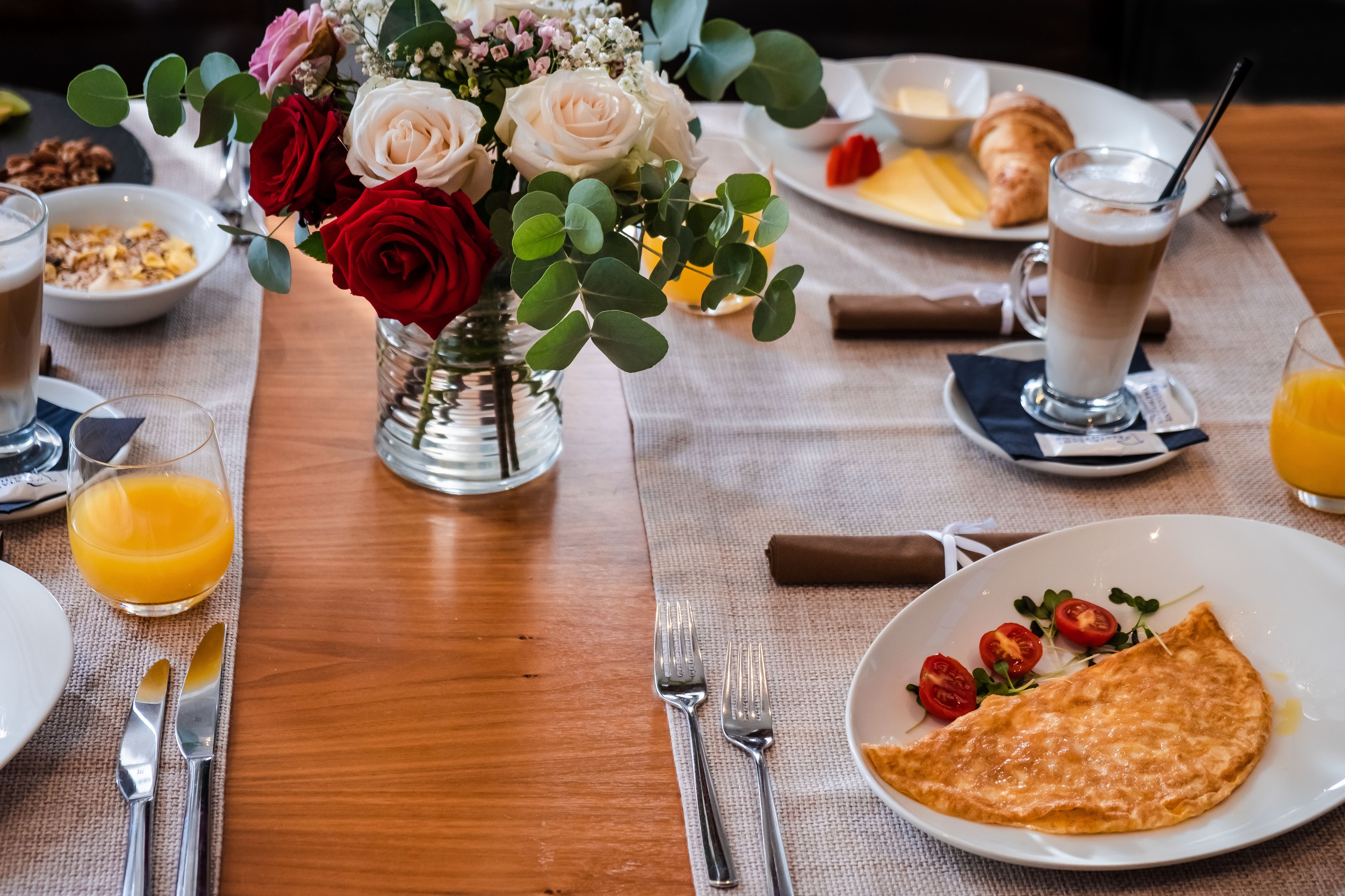 Un desayuno con un plato de tortilla, un vaso de zumo de naranja y un jarrón de flores.