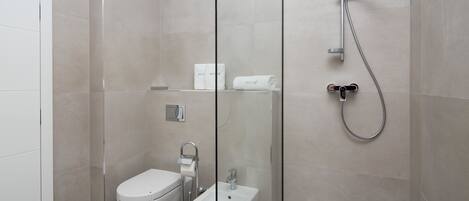 A modern bathroom with a glass partition, a bidet, a toilet, and a shower.