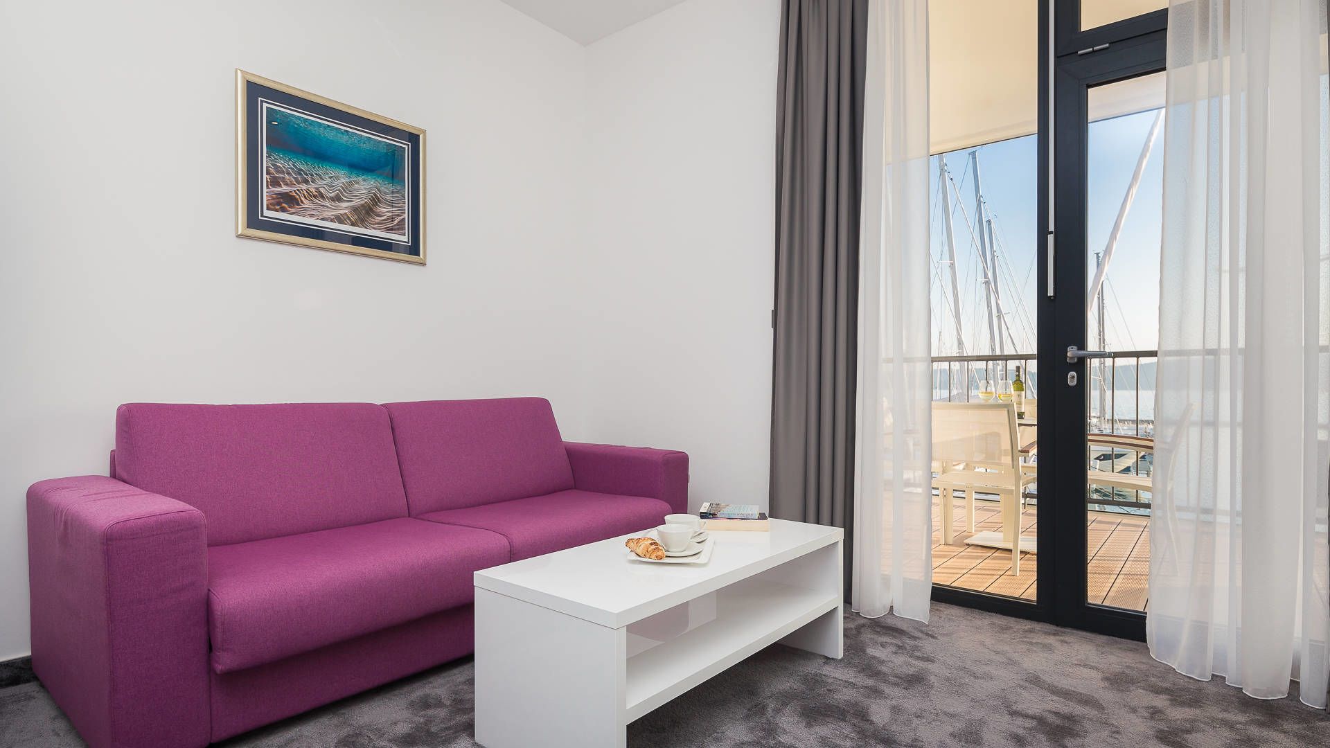 A room with a purple sofa, a white coffee table, and a framed picture on the wall.