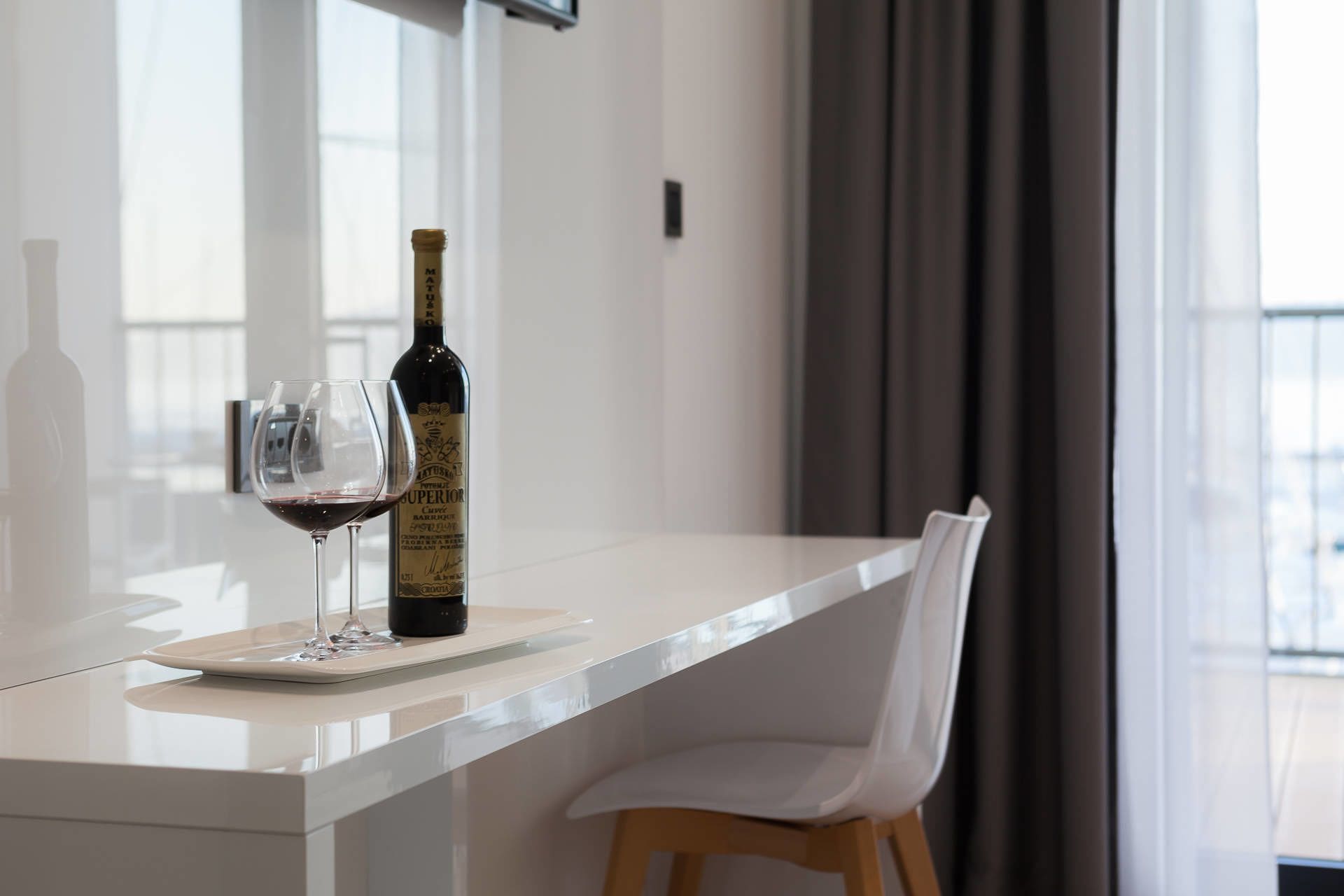 Une cuisine moderne avec un plan de travail blanc, une bouteille de vin et un verre de vin rouge.