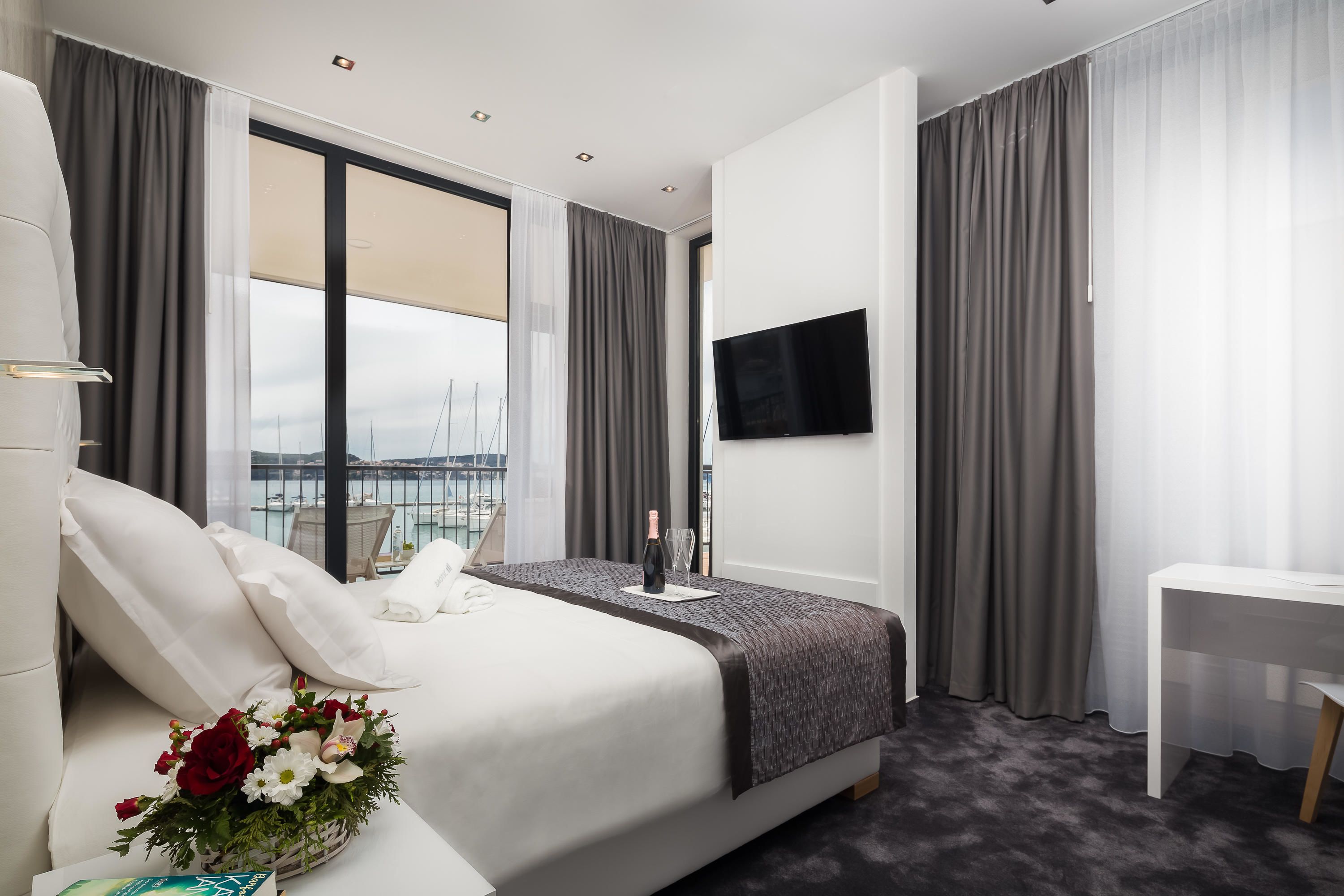 Quarto de hotel moderno com uma cama grande, uma escrivaninha, uma TV de tela plana e vista para a cidade através de amplas janelas.