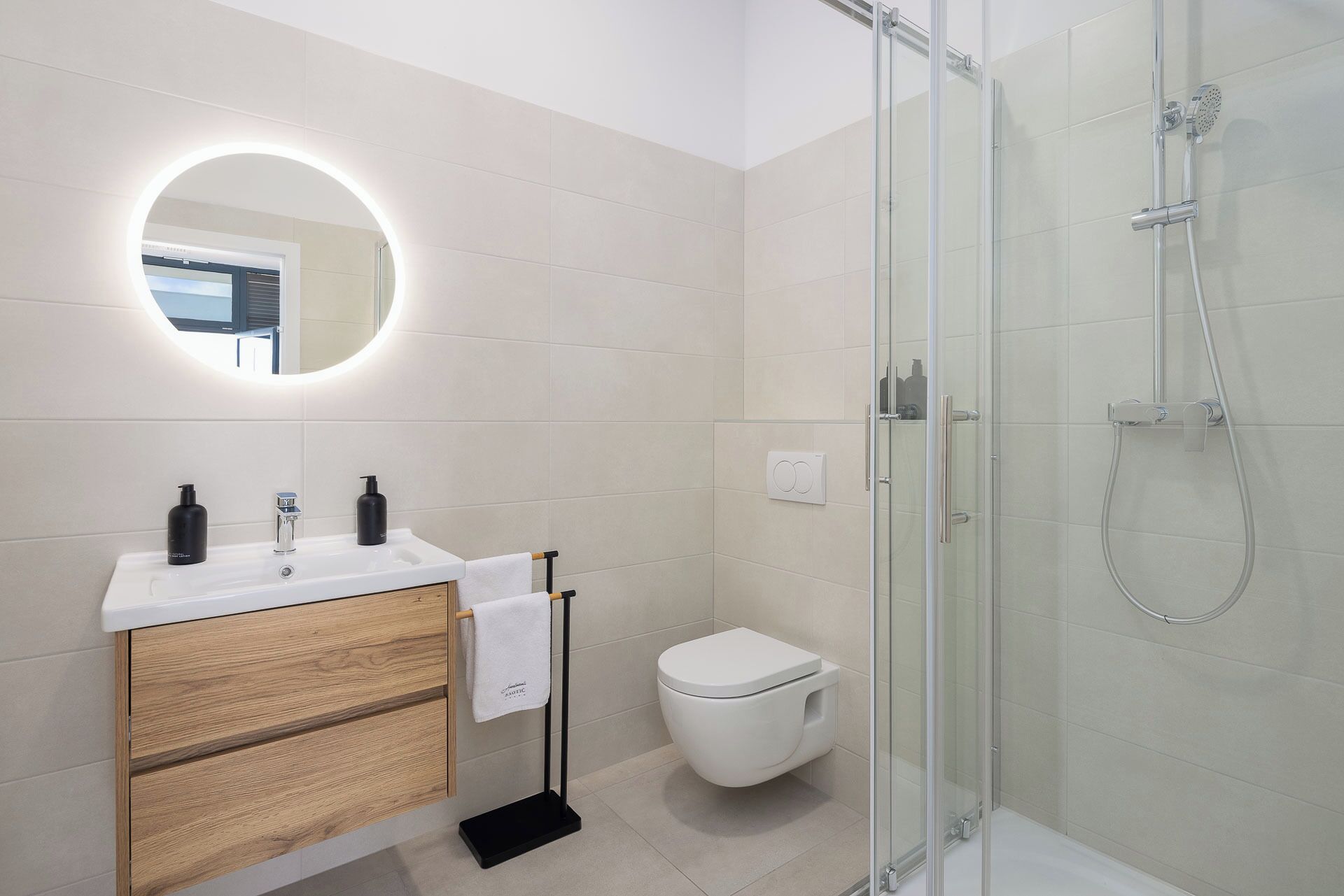 Ein modernes Badezimmer mit einer gläsernen Duschkabine, einem hölzernen Waschtisch mit weißem Waschbecken und einer Toilette.