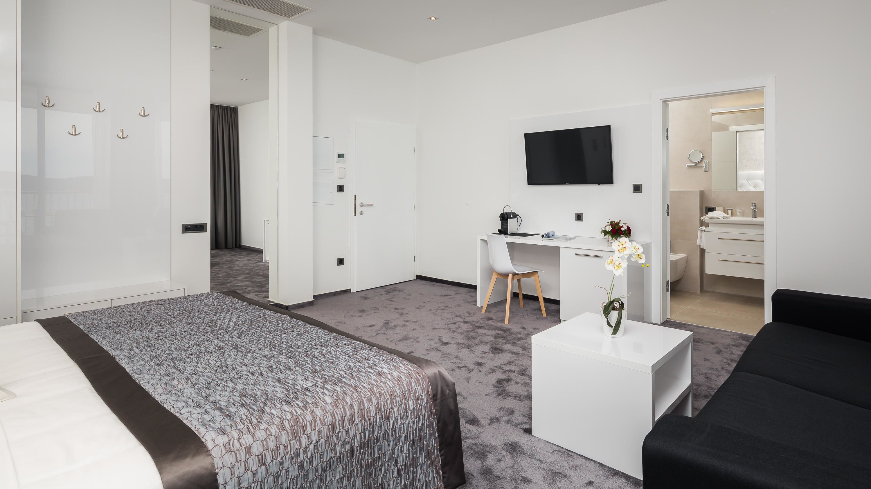 Ett modernt hotellrum med en stor säng, ett skrivbord, en platt-TV och ett badrum med spegel och handfat.