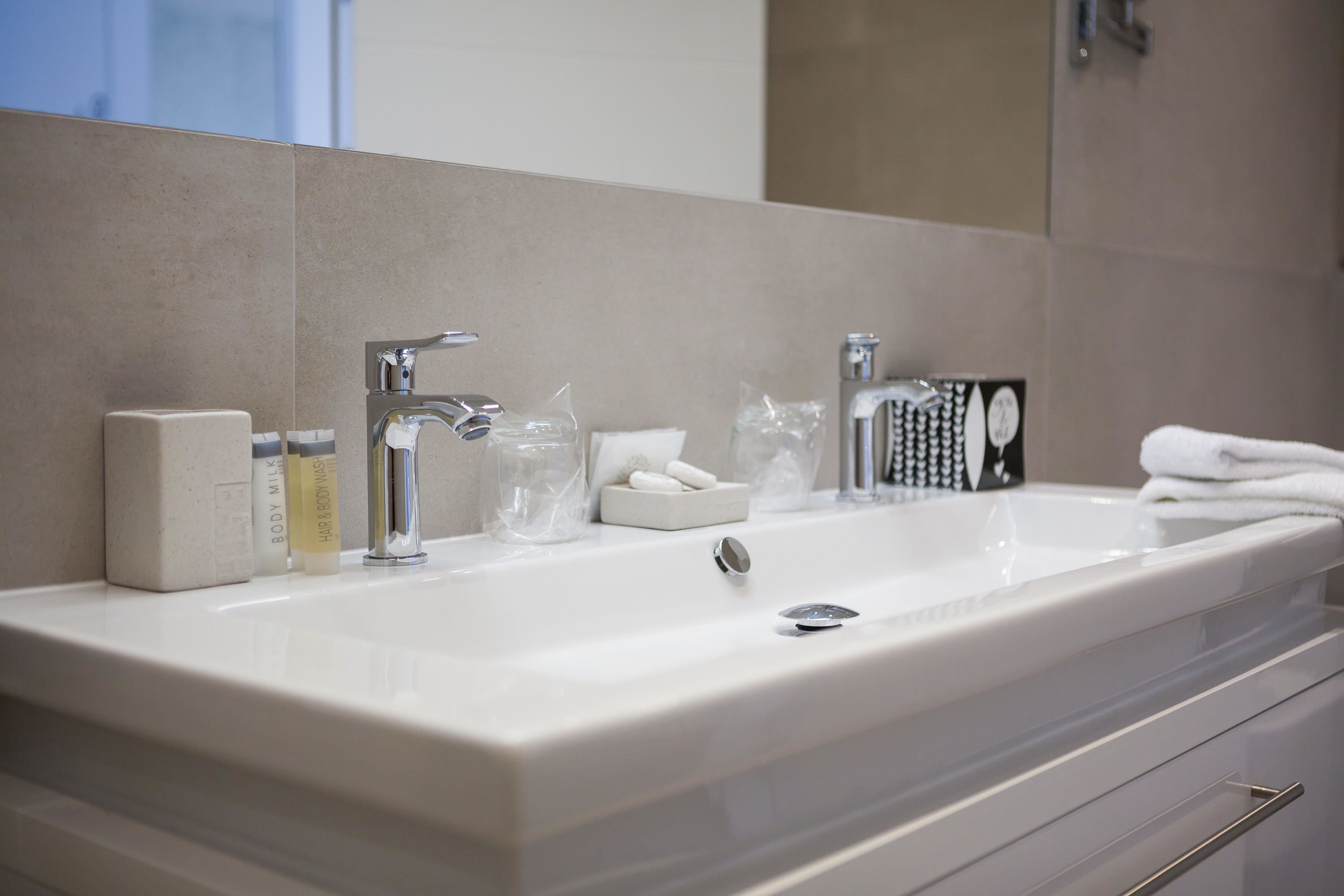 A modern bathroom with a large white sink, two faucets, and a mirror above.