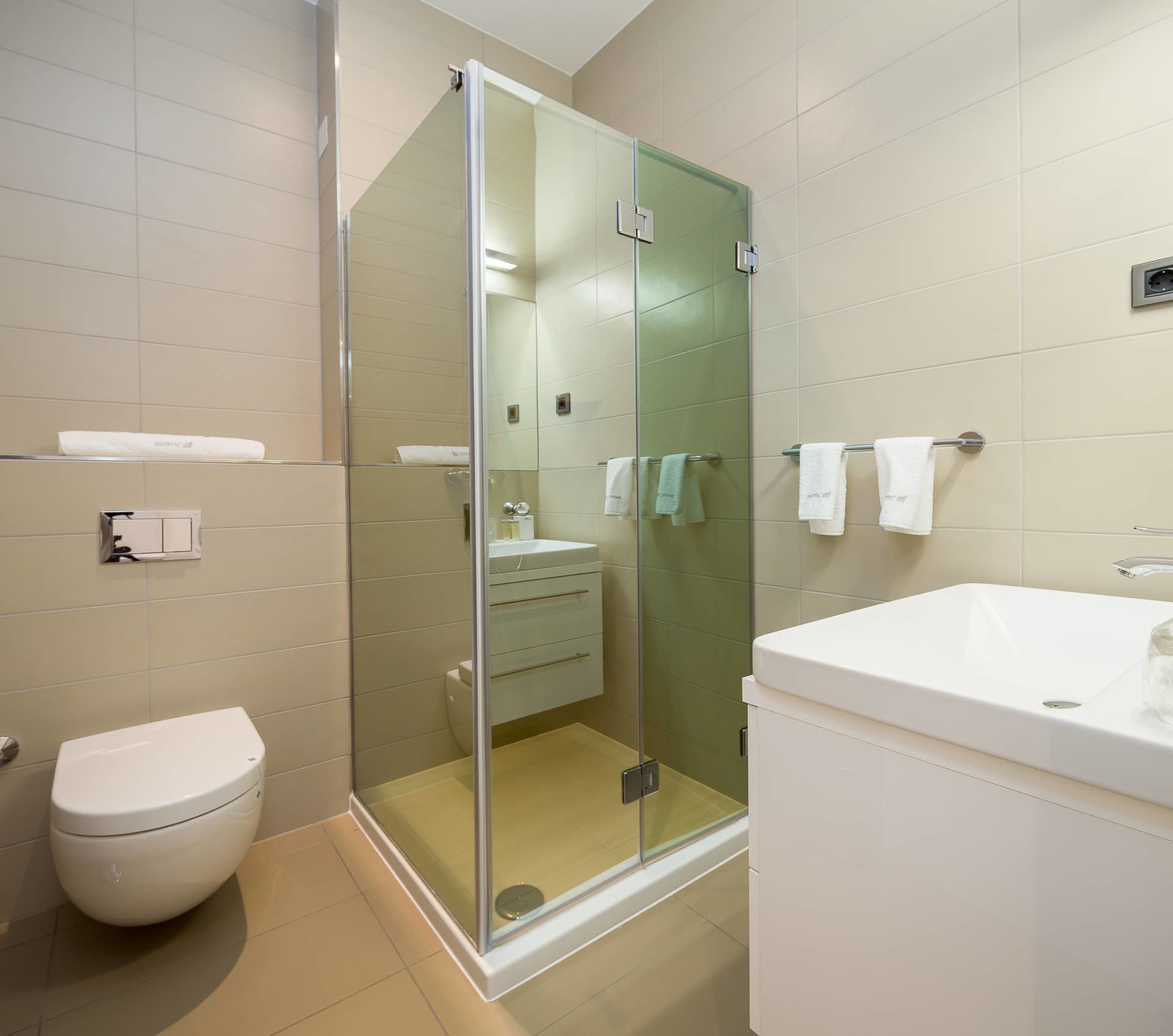 Ein modernes Badezimmer mit einer gläsernen Duschkabine, Toilette, Waschbecken und Spiegel.