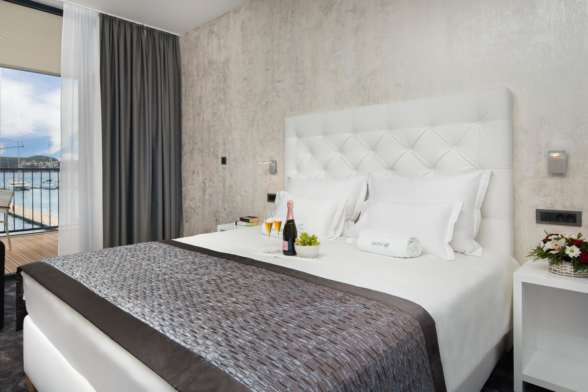 Une chambre d’hôtel moderne avec un grand lit, une vue sur la mer et un balcon équipé d’une chaise.