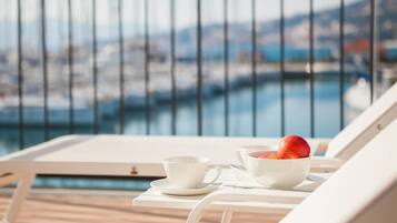 Un balcón con una mesa blanca, una taza blanca y un cuenco con fruta.
