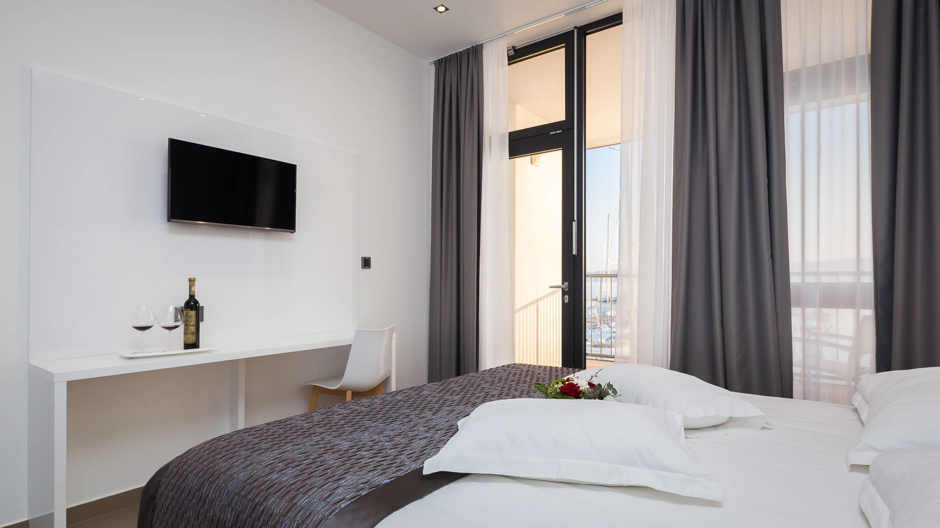 Une chambre d’hôtel moderne équipée d’un lit, d’un bureau, d’une télévision et d’un balcon avec des rideaux.