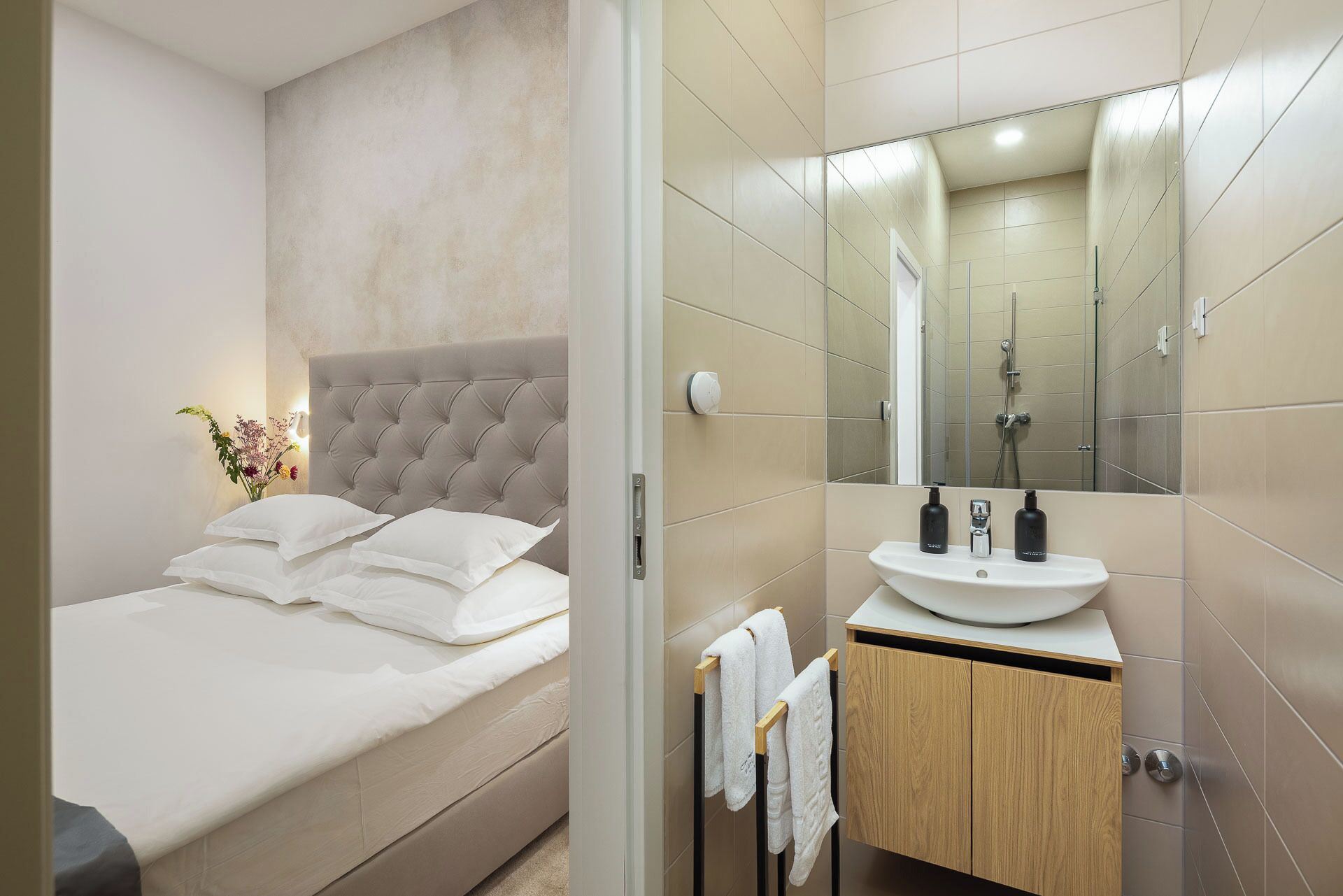 A modern bedroom with a large bed, a bedside table, and a bathroom with a sink and mirror.