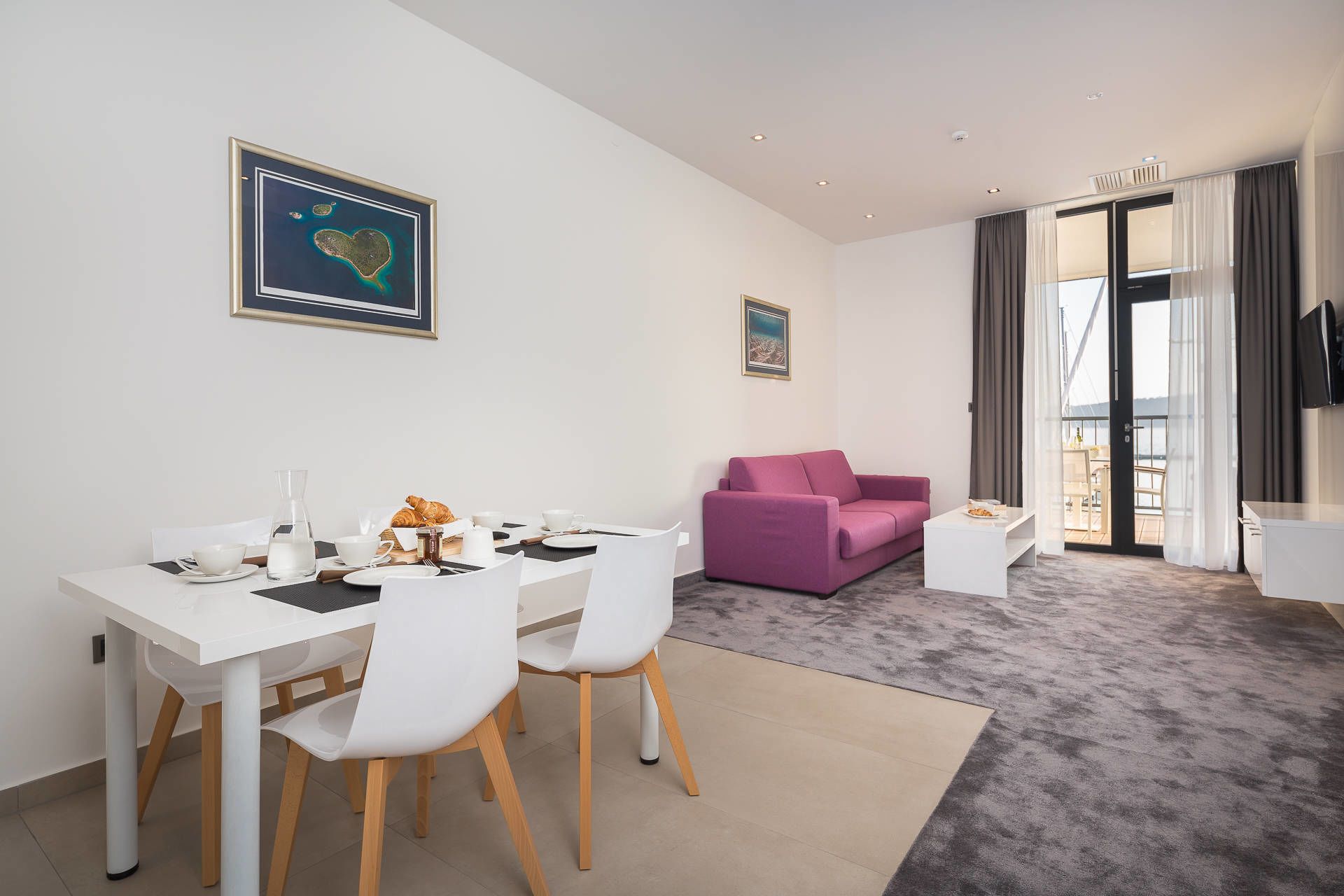 Une pièce moderne et bien éclairée, comprenant un coin repas, un canapé violet et une vue sur l’extérieur grâce à une porte vitrée.