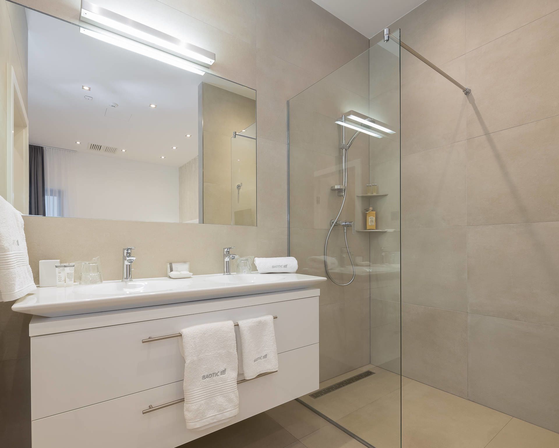 Un baño moderno con ducha de vidrio, tocador blanco con espejo y perchero para toallas.