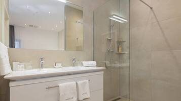 Un baño moderno con ducha de vidrio, tocador blanco con espejo y perchero para toallas.