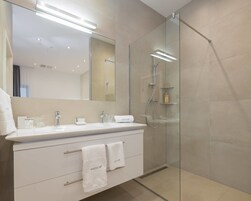 Un baño moderno con ducha de vidrio, tocador blanco con espejo y perchero para toallas.