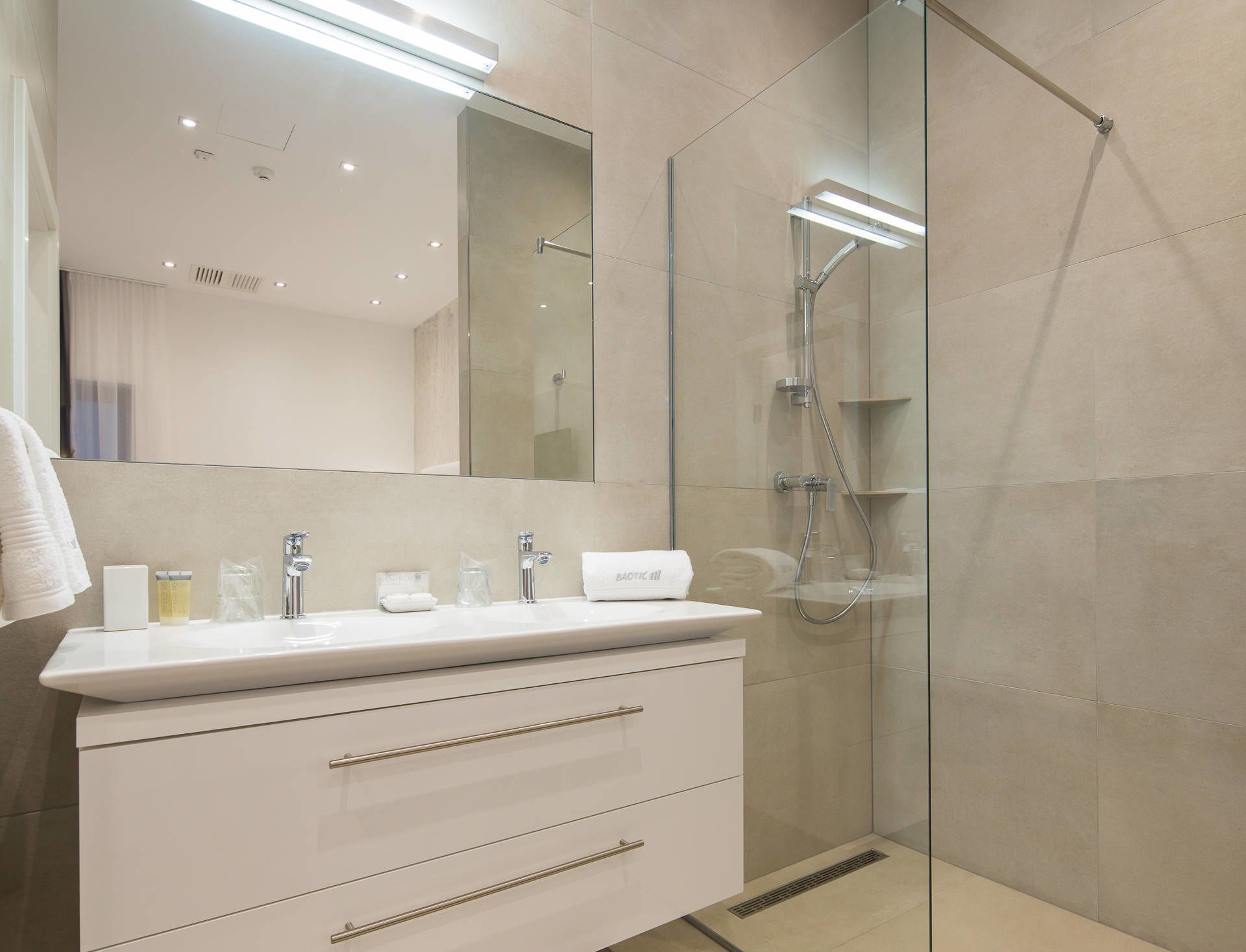 A modern bathroom with a glass-enclosed shower, a white vanity with drawers, and a large mirror above the sink.