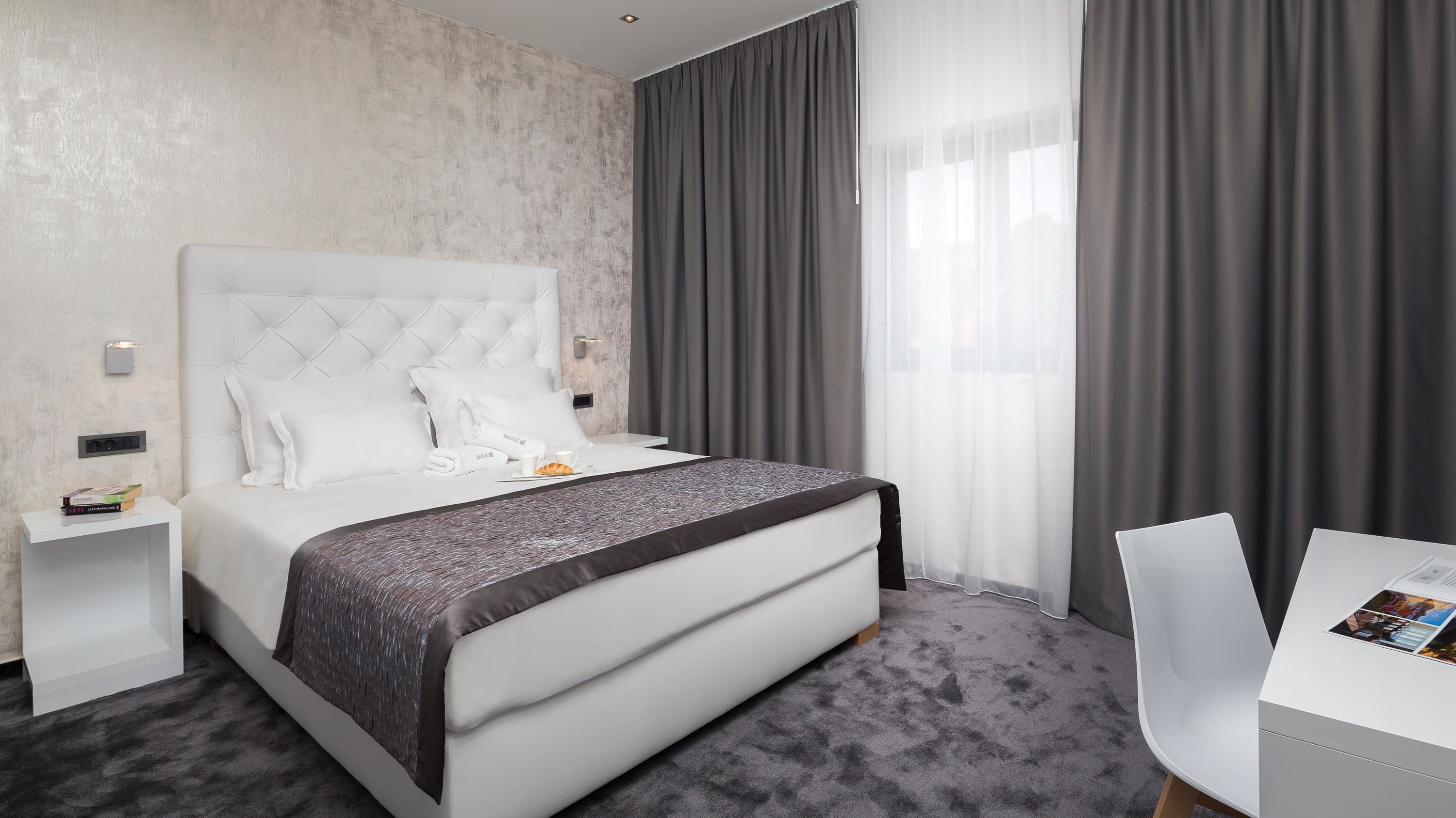 Una habitación de hotel moderna con una cama grande, una mesita de noche, una silla y una pequeña mesa con una computadora portátil.