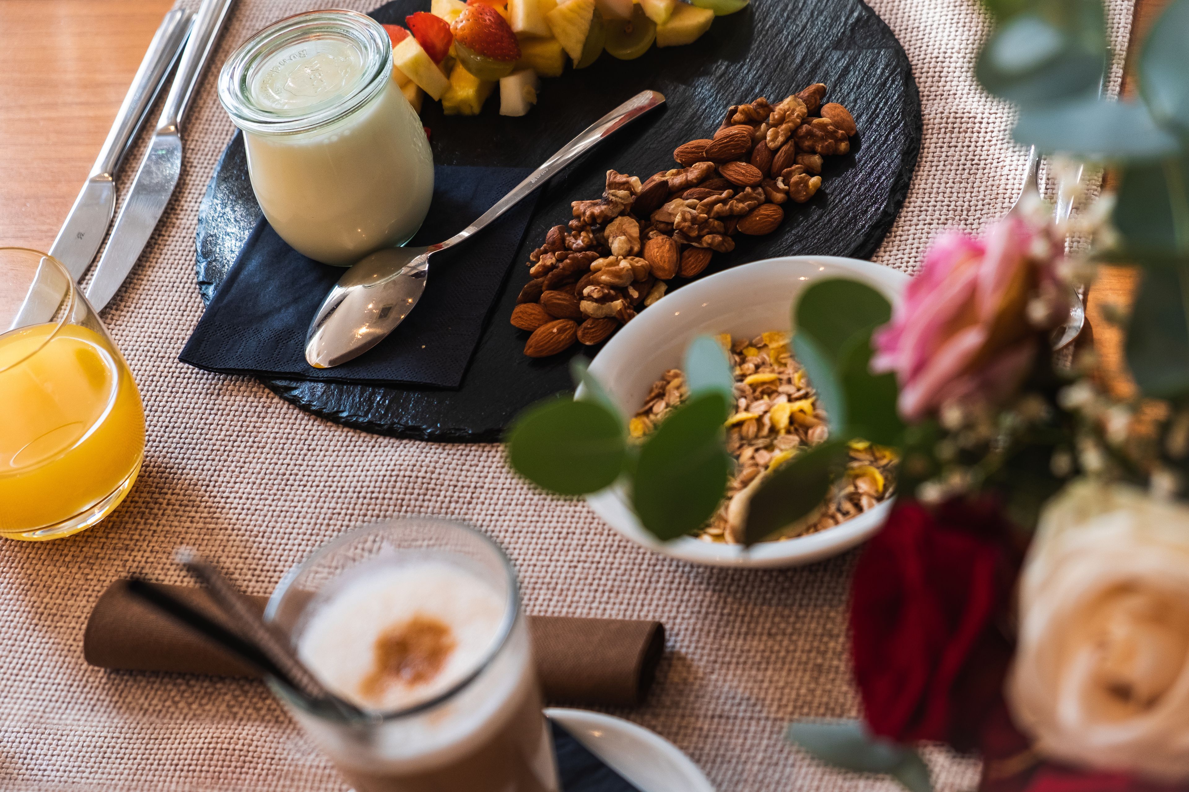 A breakfast setting with a plate of fruits, a bowl of granola, a glass of orange juice, and a jar of yogurt.