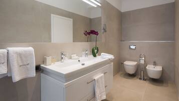 A modern bathroom with a large mirror, a white vanity, a bidet, and a towel rack.