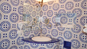 Un baño con pared de azulejos estampados, un lavamanos, un espejo, un perchero para toallas y un cabezal de ducha de mano.