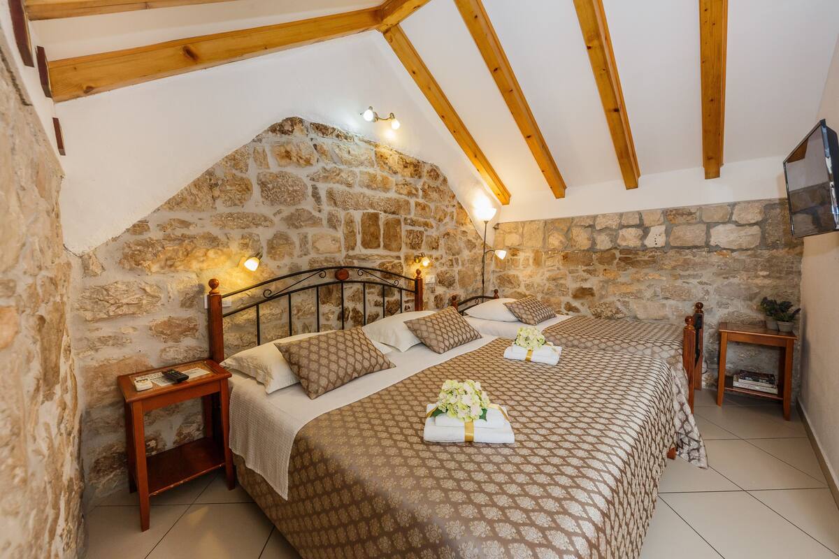 A bedroom with a stone wall, wooden beams, a bed with patterned bedding, and bedside tables.