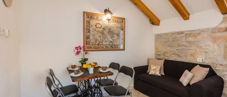 Un comedor con una mesa lista para dos personas, un sofá negro y una pared de piedra.