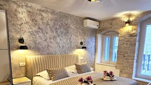 A bedroom with a bed, bedside lamps, a stone wall, and a window.
