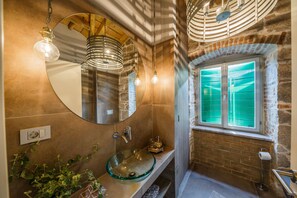 A bathroom with a glass vessel sink, a round mirror, and a window with green-tinted glass. - Villa Spaladium (Split)