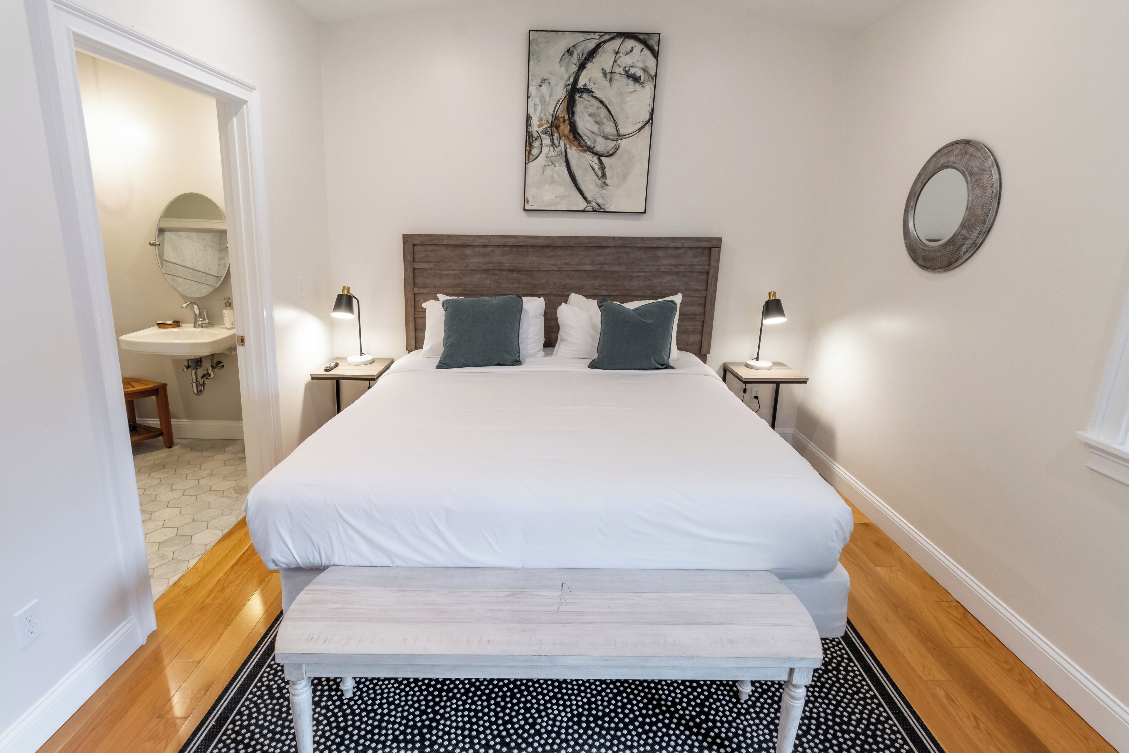 A neatly arranged bedroom with a large bed, bedside lamps, a bedside table, and a wall-mounted mirror.