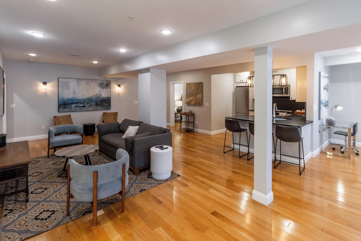A spacious living area with a sofa, chairs, and a coffee table. There is a kitchen area with a dining table and chairs.