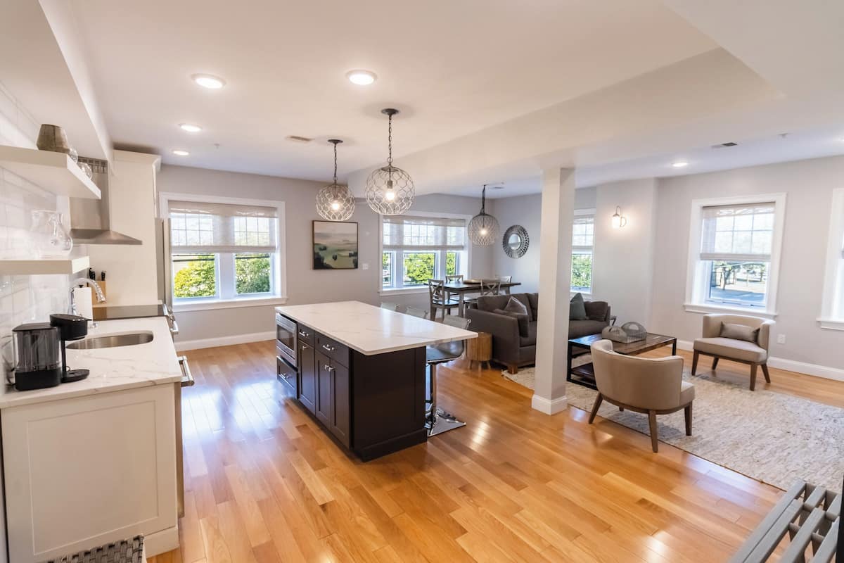 A spacious kitchen with a central island, wooden flooring, and pendant lighting.
