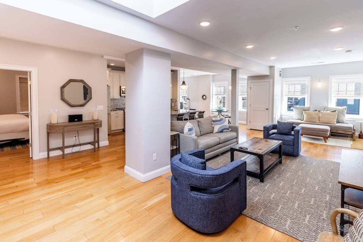 A spacious living area with a wooden floor, a gray sofa, a blue armchair, and a coffee table.