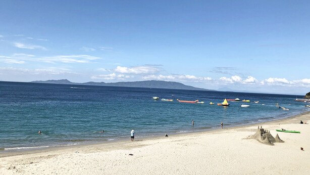 Une plage avec un ciel dégagé, une eau calme et des montagnes à l’horizon.