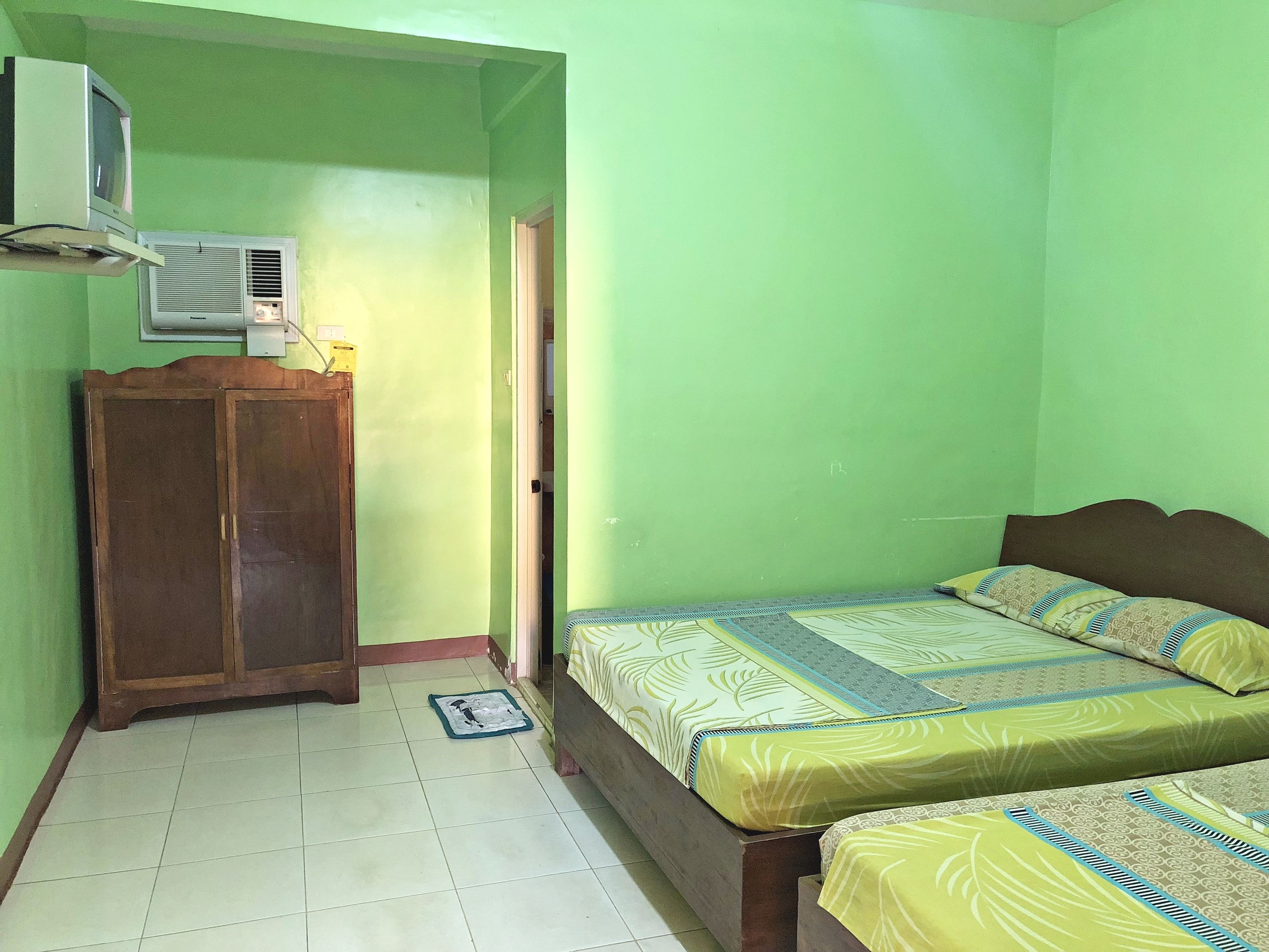 A room with two beds, a wooden wardrobe, and an air conditioner mounted on the wall.