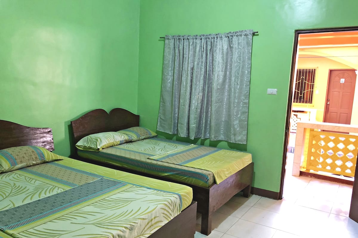 A room with two beds, a window with curtains, and a door leading to an outdoor area.