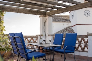 A terrace with blue chairs, a table, and a bottle of wine. - Hotel Los Castaños (Cartajima)