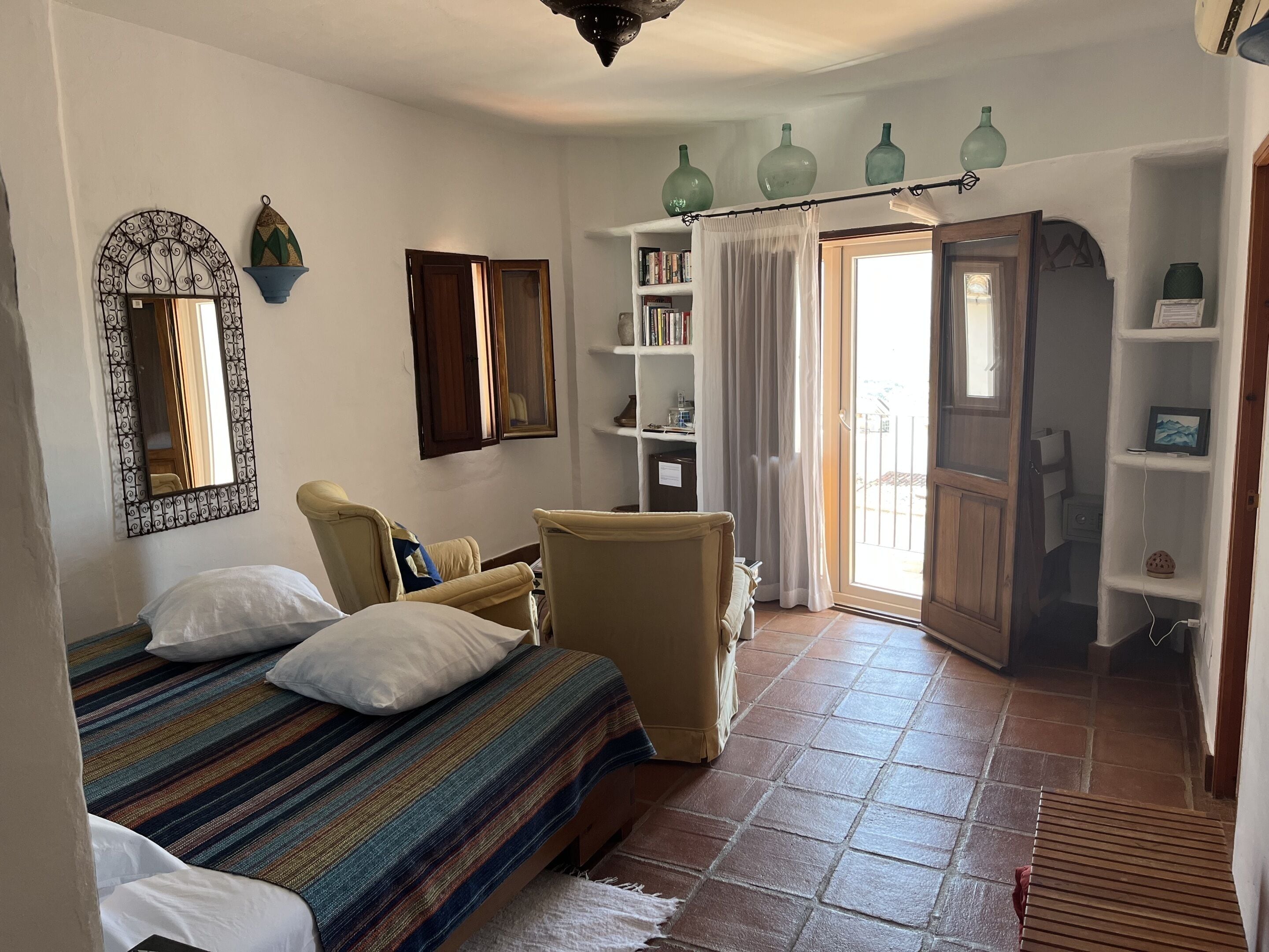 A bedroom with a bed, a chair, a bookshelf, and a sliding door to a balcony.