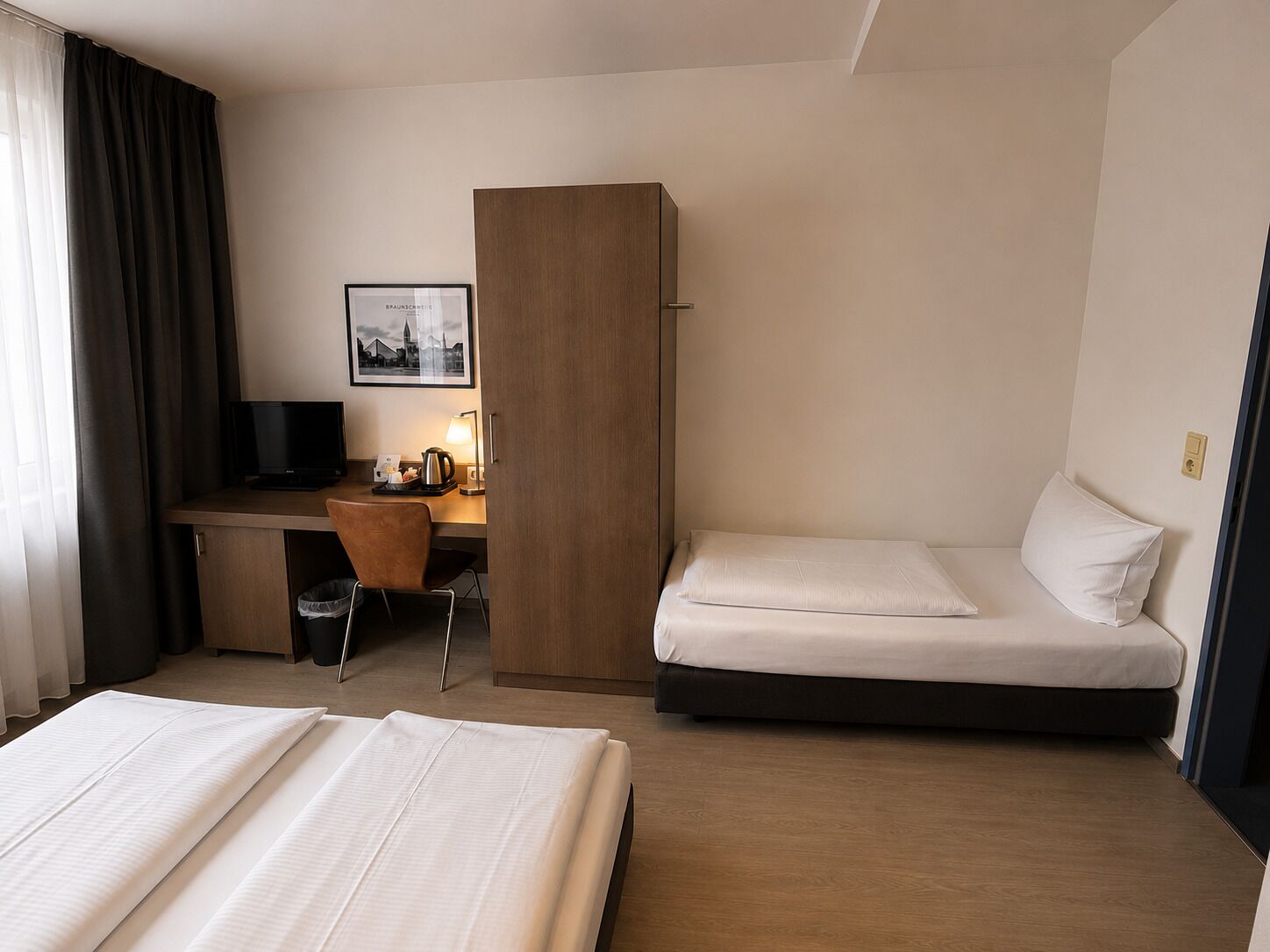 Una habitación de hotel con una cama, un escritorio con silla, televisión y un cuadro en la pared.