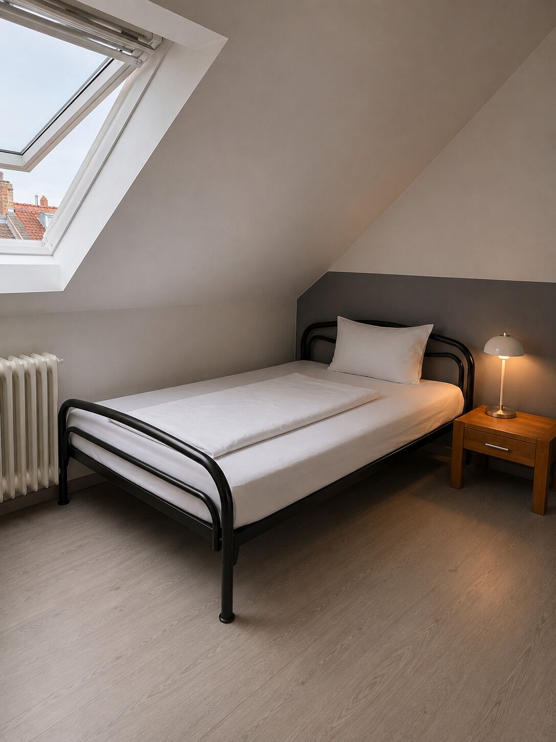 Et lille enkeltværelse med skydelugt, et sengebord med lampe og en radiator.