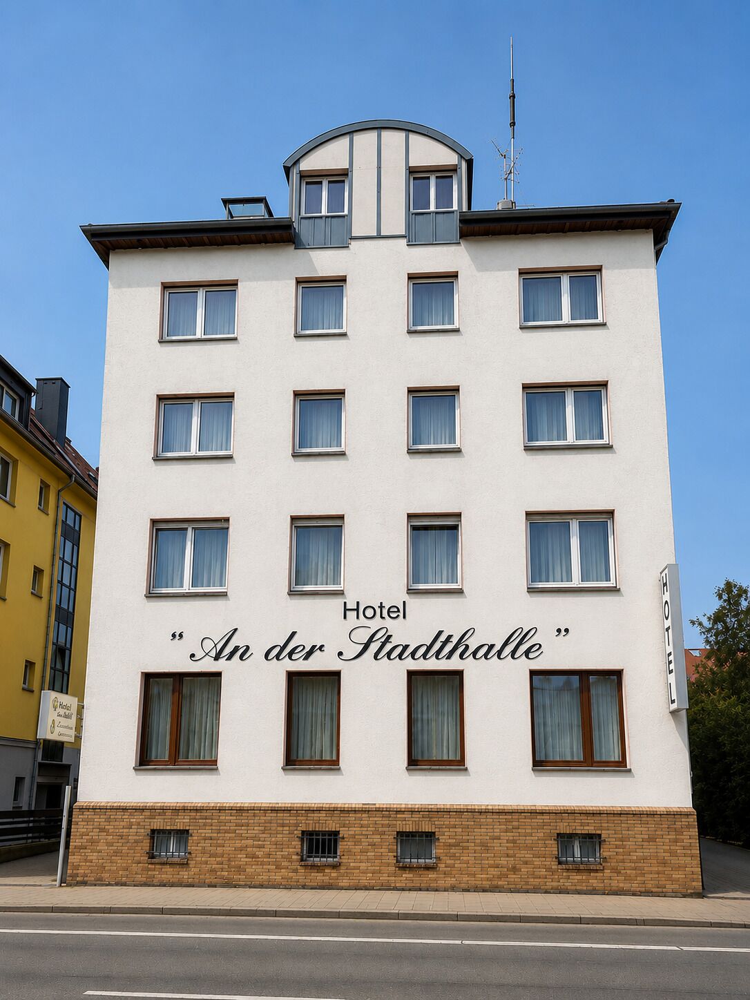 Un edificio de hotel con múltiples ventanas, un letrero que dice 'Hotel An der Stadthalle' y una base de ladrillo.