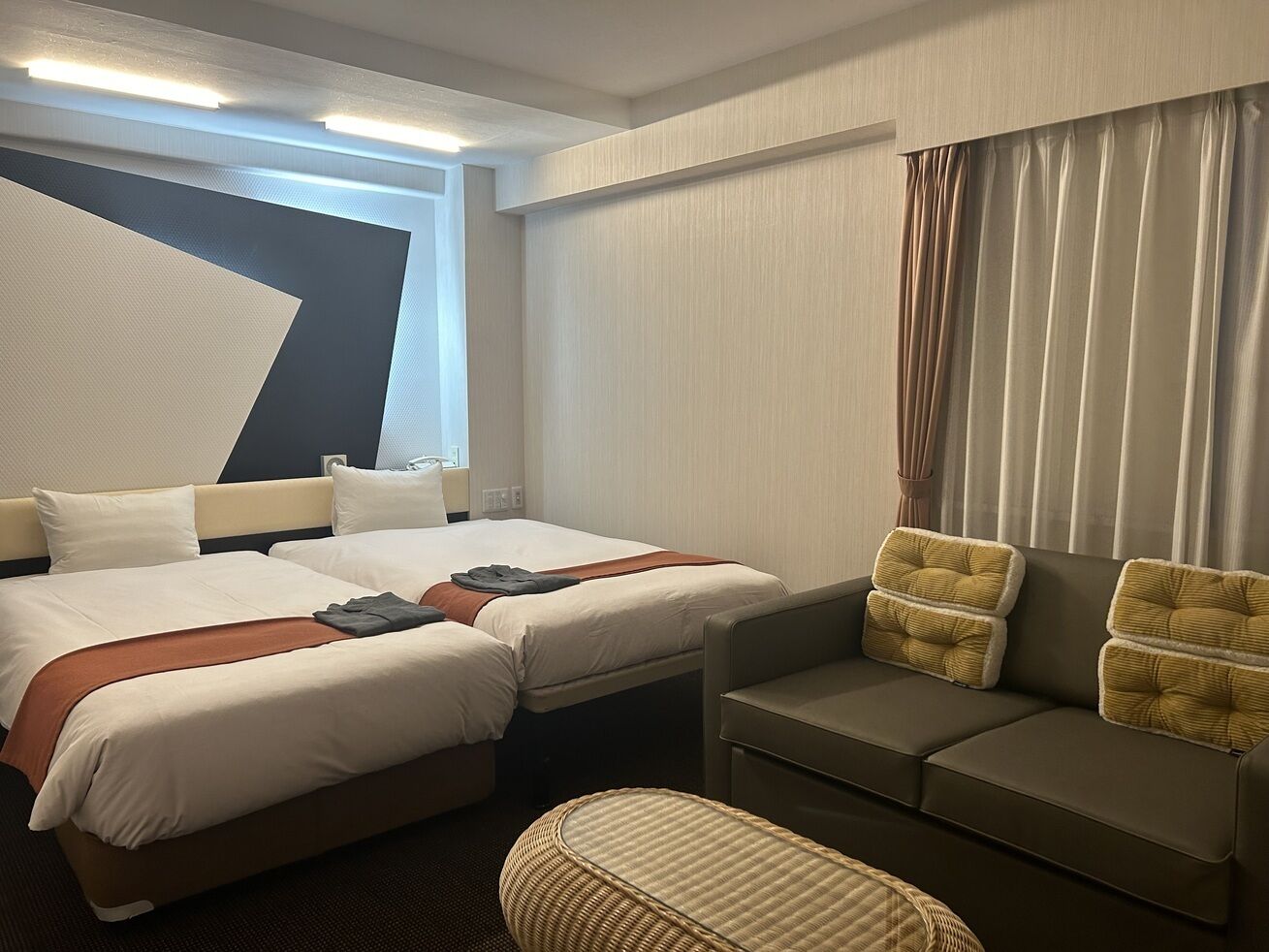 A hotel room with two beds, a sofa, a chair, and a large window.