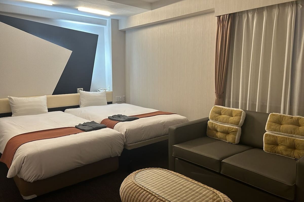 A hotel room with two beds, a sofa, a chair, and a large window.