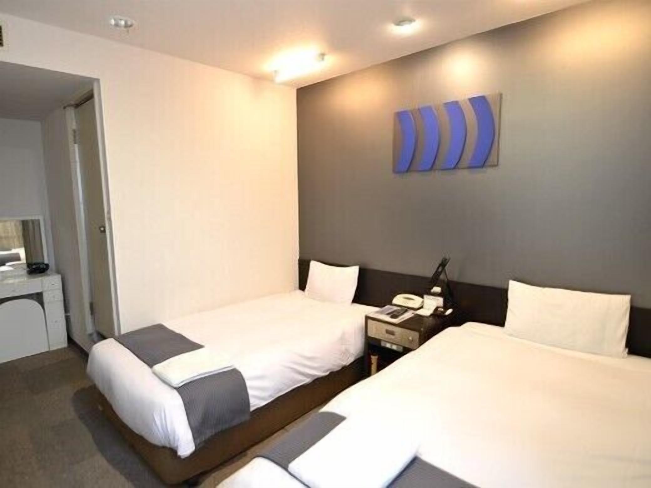 A hotel room with two beds, a desk, and a wall-mounted phone.