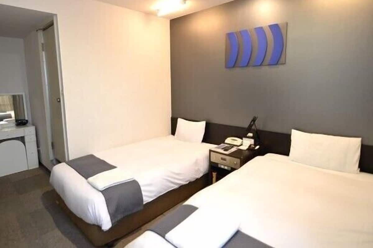 A hotel room with two beds, a desk, and a wall-mounted phone.