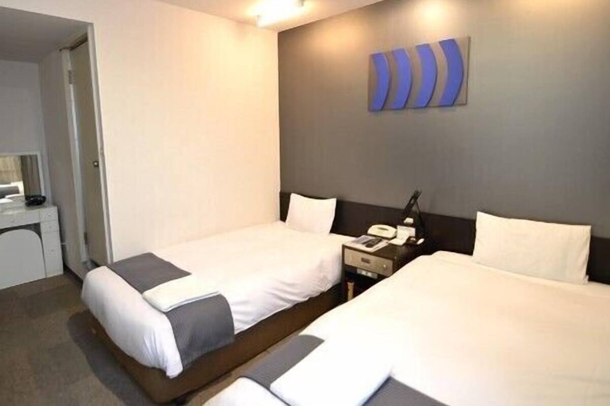Habitación de hotel con dos camas, un escritorio y teléfono en la pared.