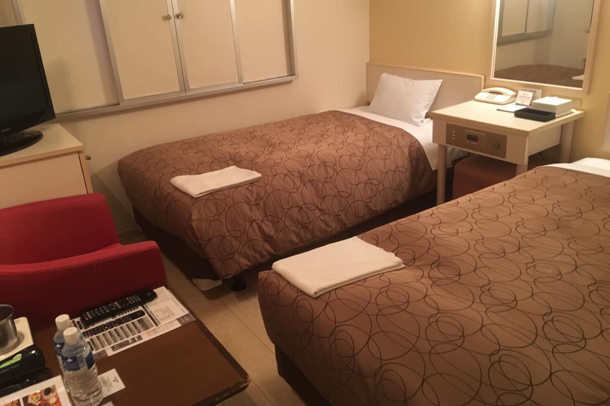 A hotel room with two beds, a desk, a chair, a television, and a mirror.