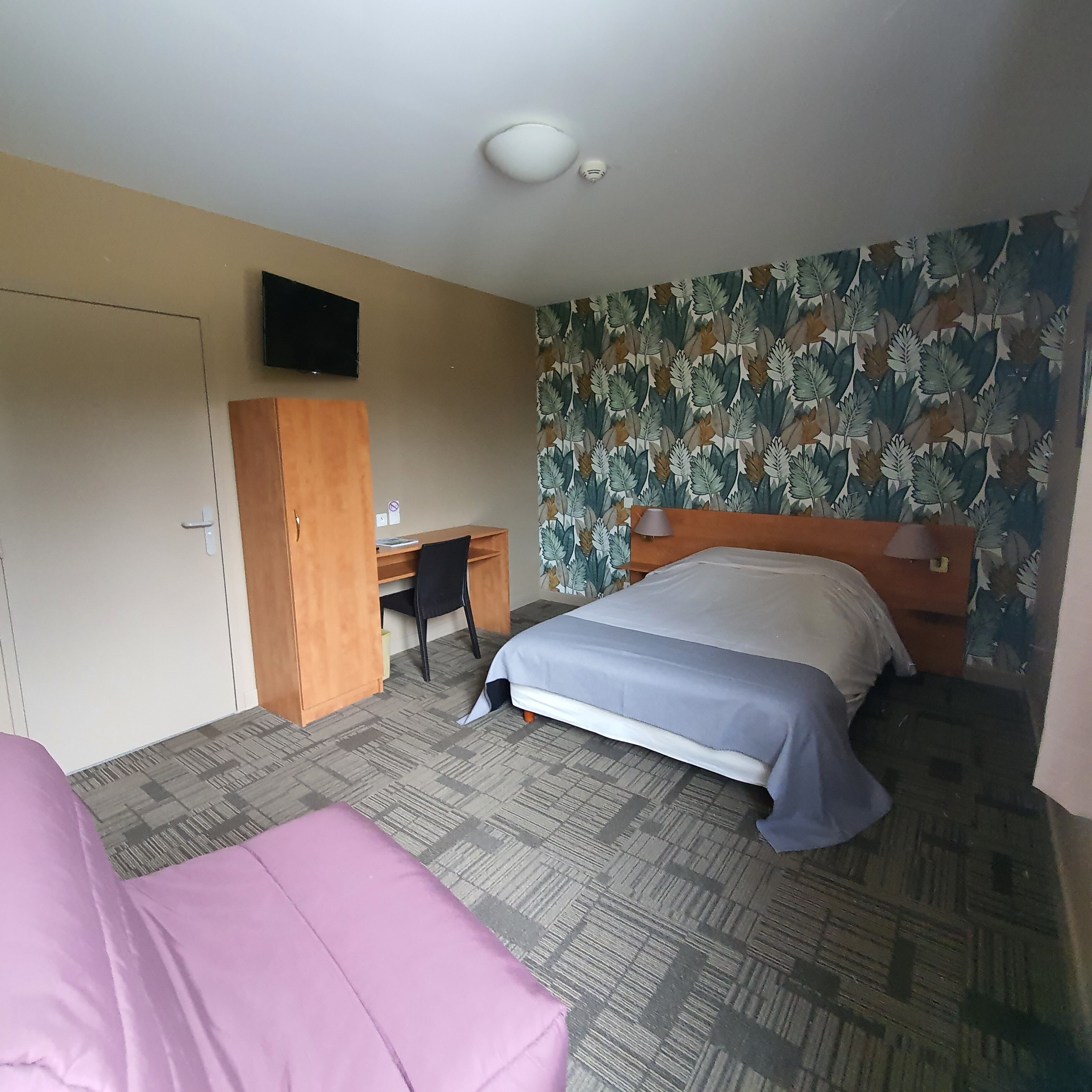 A hotel room with a bed, a desk, a chair, and a television on the wall.