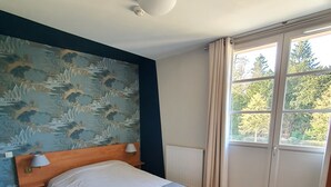 Ett hotellrum med en säng, en sänggavel, ett nattduksbord, en lampa, ett element och ett fönster med gardiner.