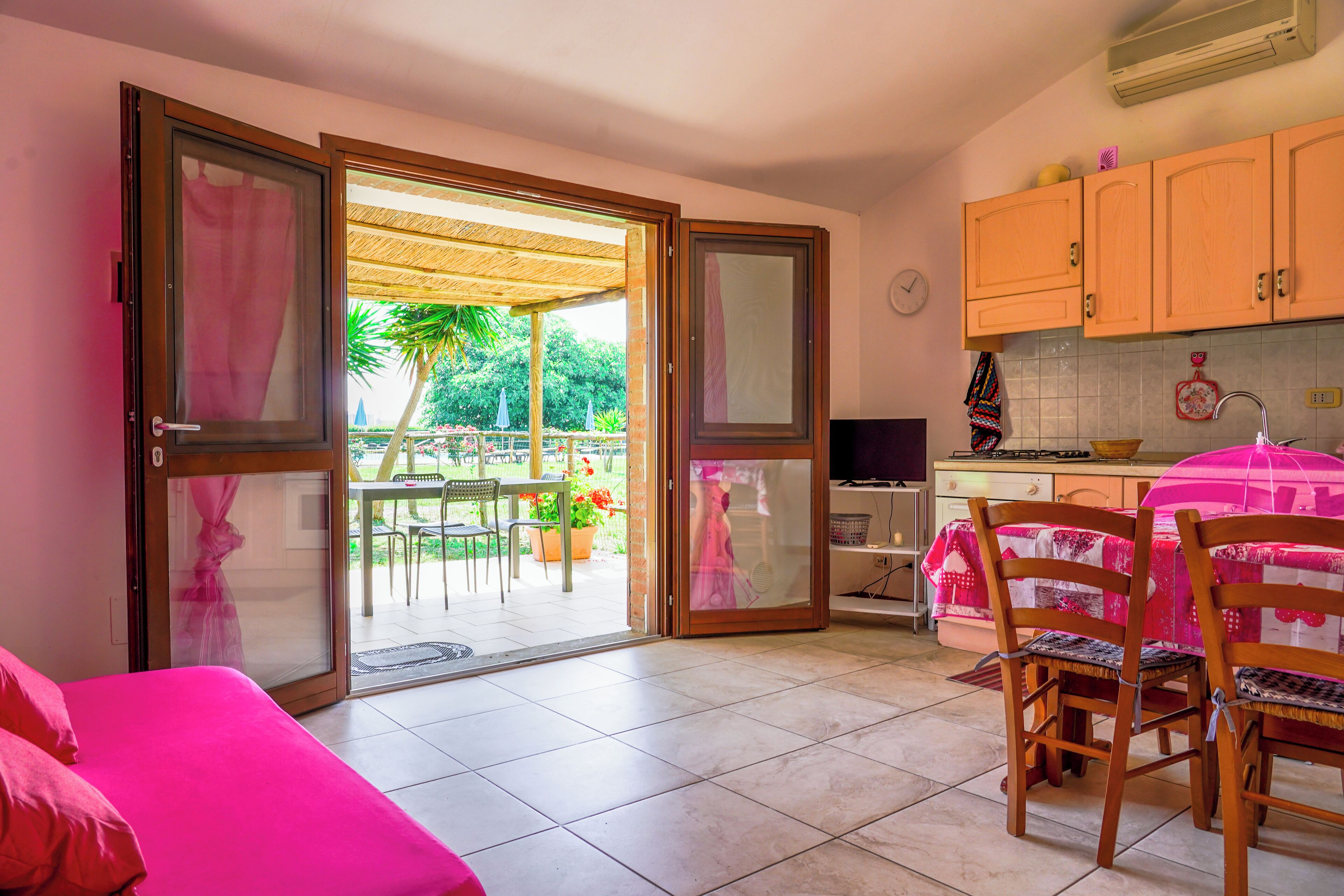 A room with a bed, a table with chairs, a kitchen area, and a sliding glass door leading to an outdoor patio.
