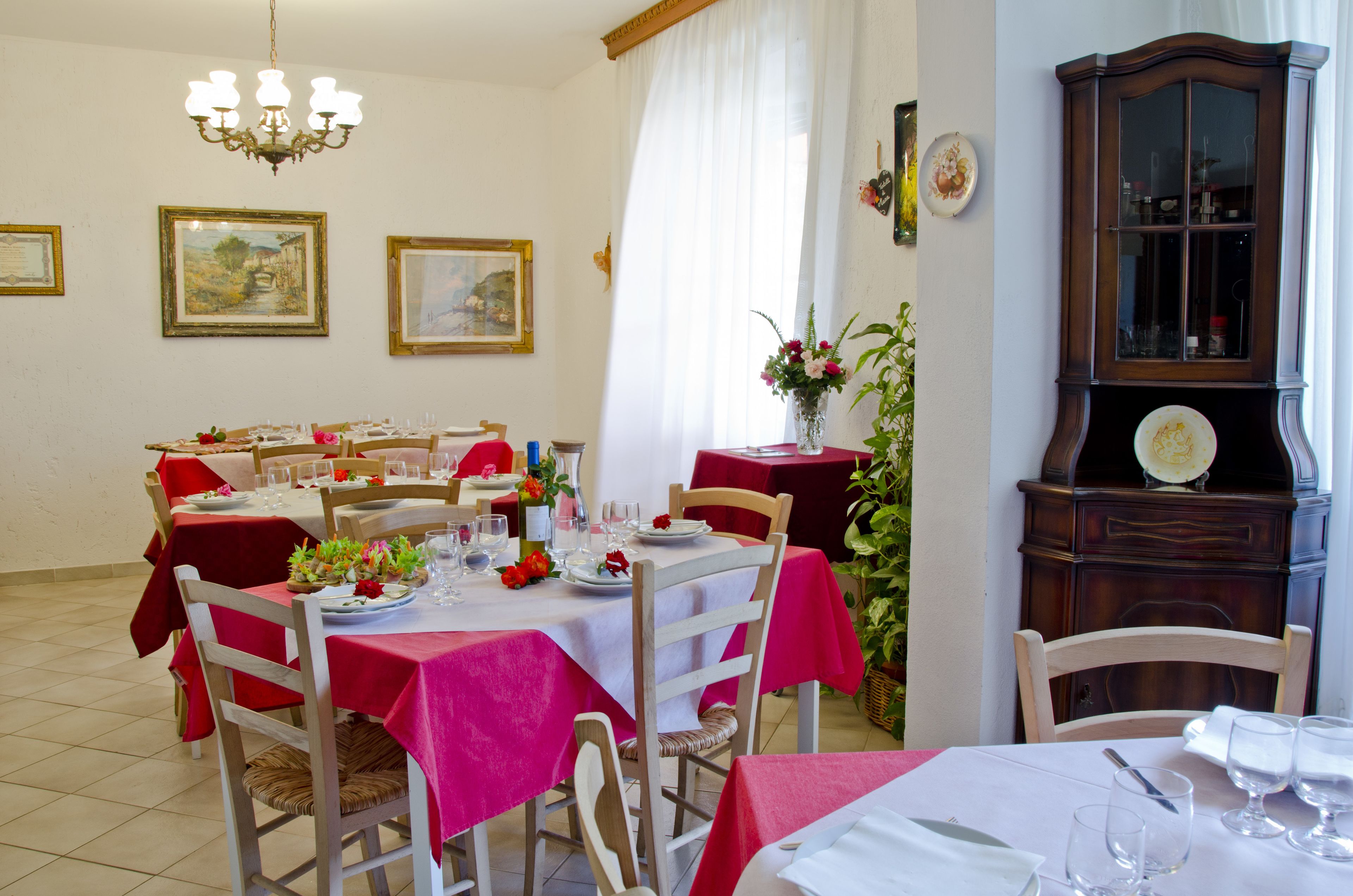 A dining area with tables set for a meal, featuring red tablecloths and white chairs.