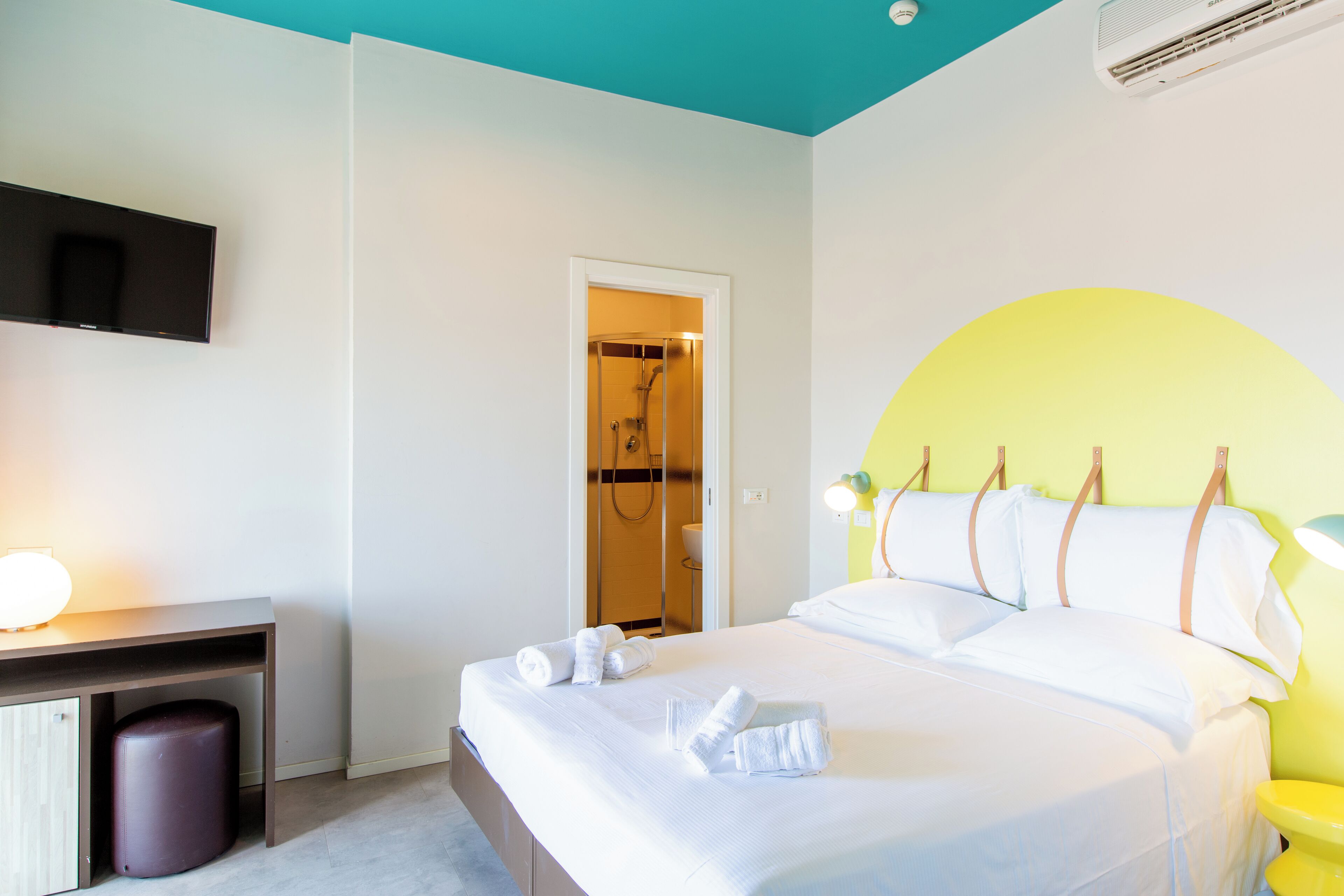 A hotel room with a bed, a desk, a TV, and a shower area.